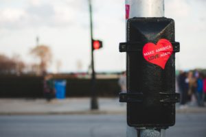 heart-shaped sticker on traffic pole with the words Make America Love Again on it, photo by Kayle Kaupanger
